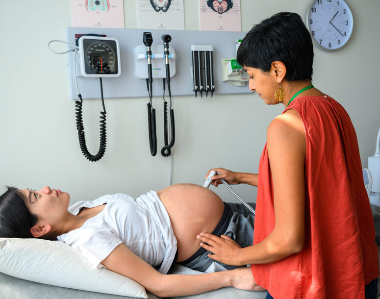 A pregnant woman laying down in a doctors office, while a healthcare provider takes an ultrasound